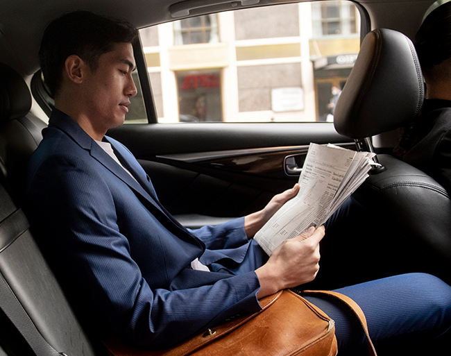 Executive passenger reading newspaper in car backseat
